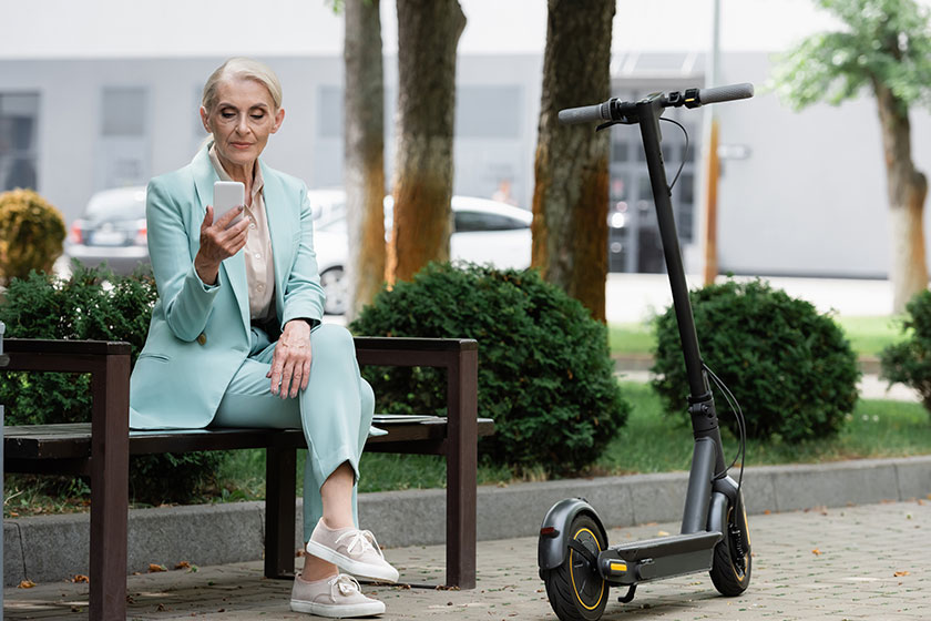 Senior businesswoman using smartphone while sitting bench electric kick scooter Senior businesswoman using smartphone while sitting bench electric kick scooter