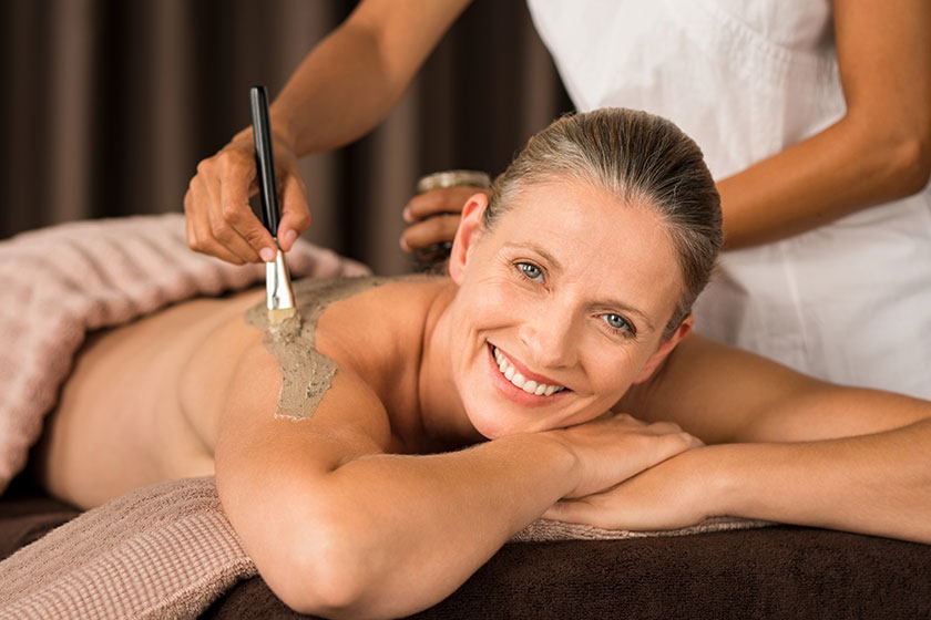 Smiling senior woman looking camera while beautician getting mud mask Smiling senior woman looking camera while beautician getting mud mask