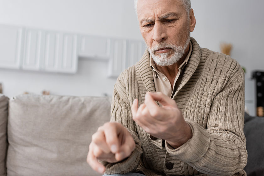 Worried senior man suffering parkinsonian syndrome looking trembling hands blurred Worried senior man suffering parkinsonian syndrome looking trembling hands blurred