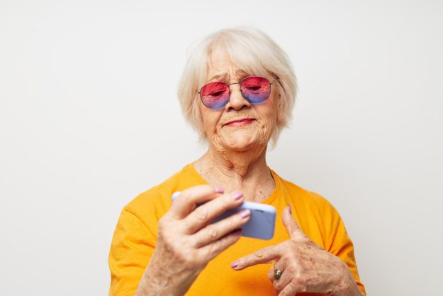 Photo of retired old lady in fashionable glasses with a smartphone in hand cropped view Photo of retired old lady in fashionable glasses with a smartphone in hand cropped view
