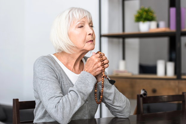 senior woman holding wooden rosary praying