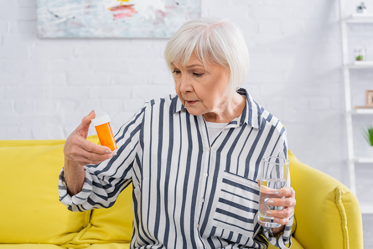 senior woman looking jar pills holding glass water