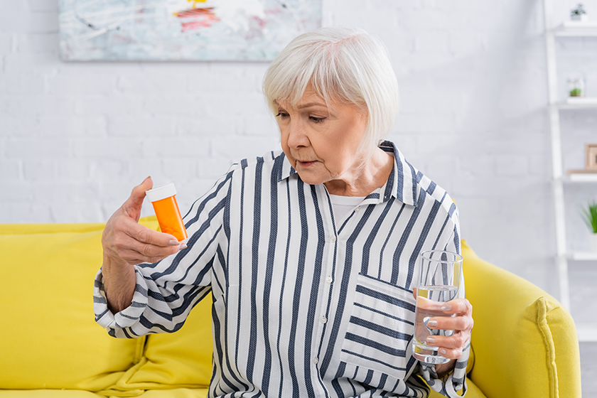 senior woman looking jar pills holding glass water senior woman looking jar pills holding glass water