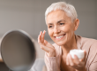 gorgeous mature woman applying facial moisturizer