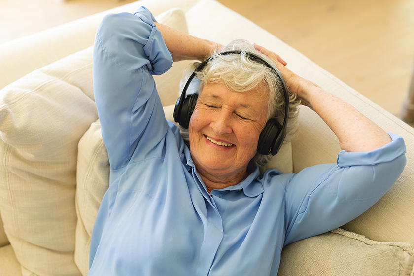senior caucasian woman sitting sofa wearing headphones
