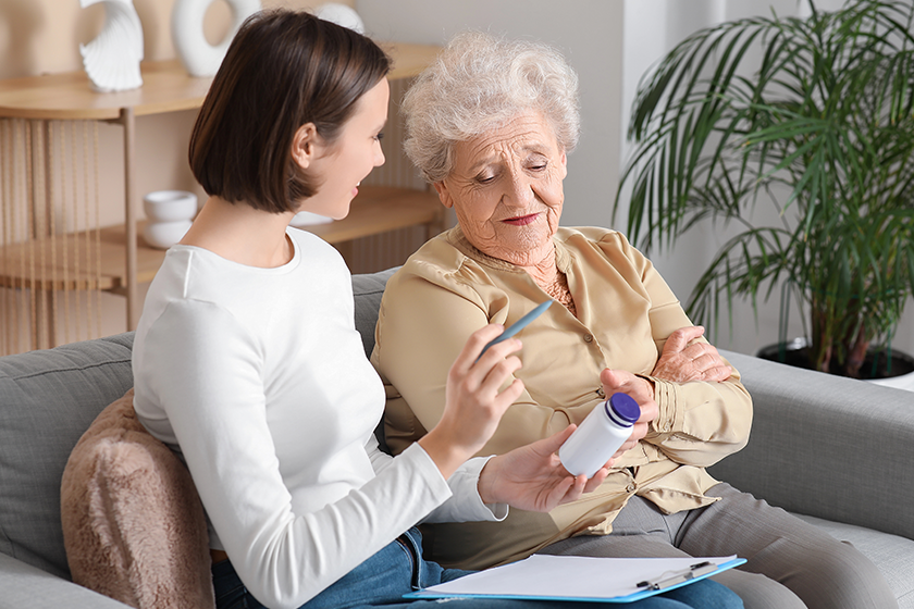 young nurse giving pills senior woman sofa