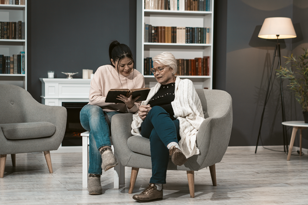 young woman reads book for her elderly mother young woman reads book for her elderly mother